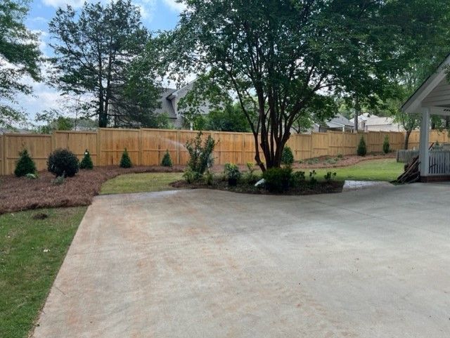 a driveway with a wooden fence and a gazebo in the background