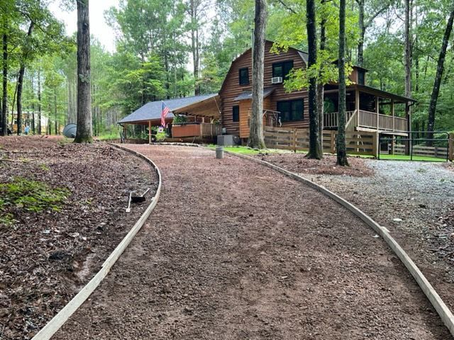 a log cabin is surrounded by trees and a dirt road leading to it