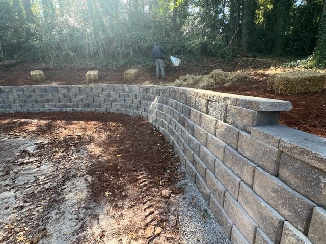 a man is standing next to a brick wall in a field