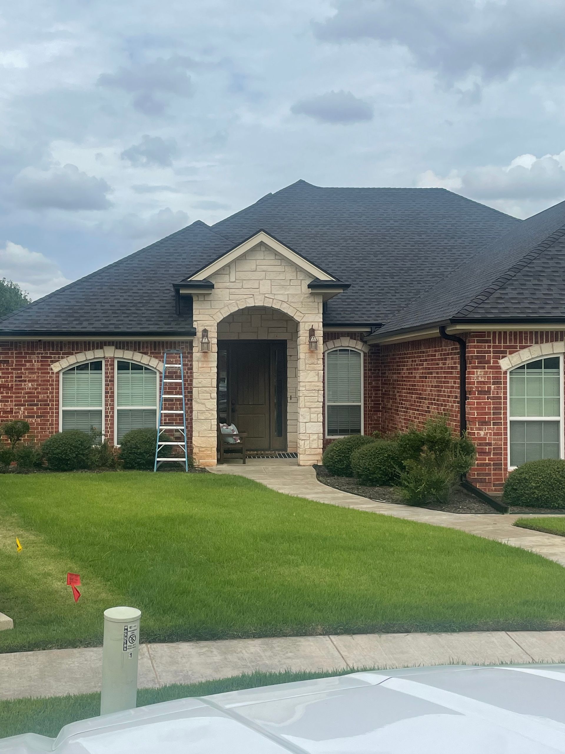 Brick house with dark roof and green lawn; ladder near front door.