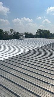 A metal roof is being painted white on a sunny day
