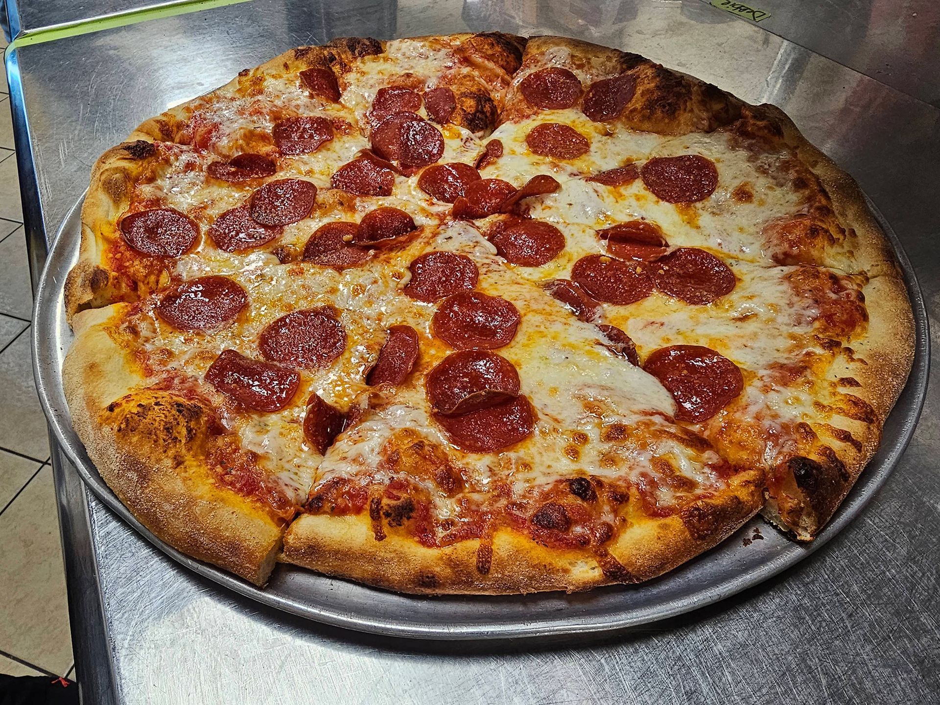 A pepperoni pizza is sitting on a metal pan on a table.