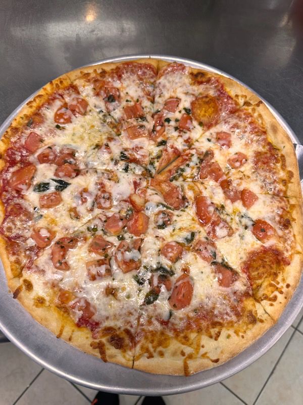 A pizza with tomatoes and cheese is on a metal pan.