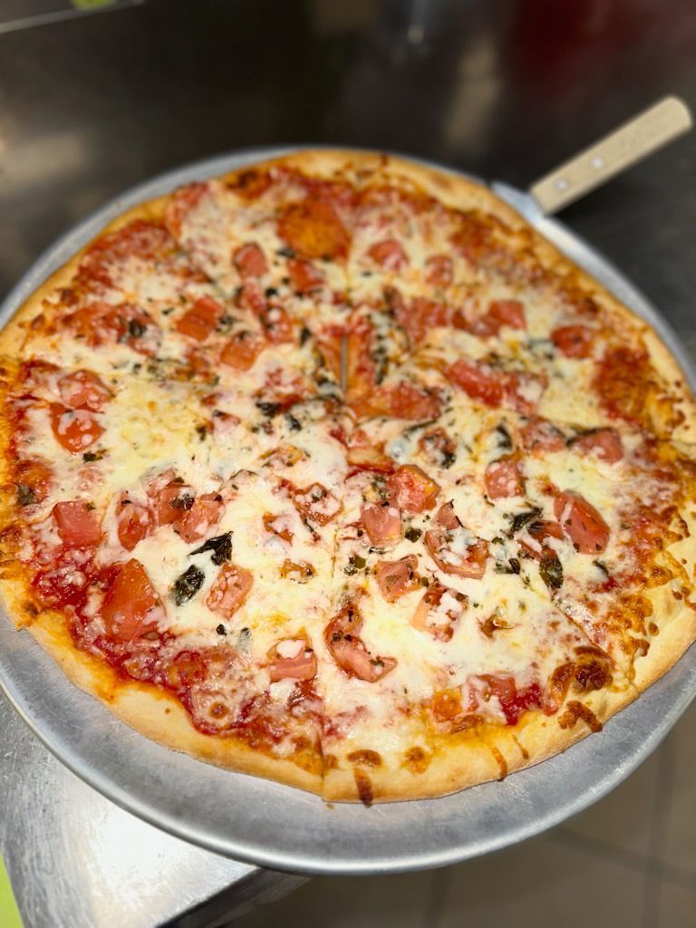 A pizza with tomatoes and cheese on a pan on a table.