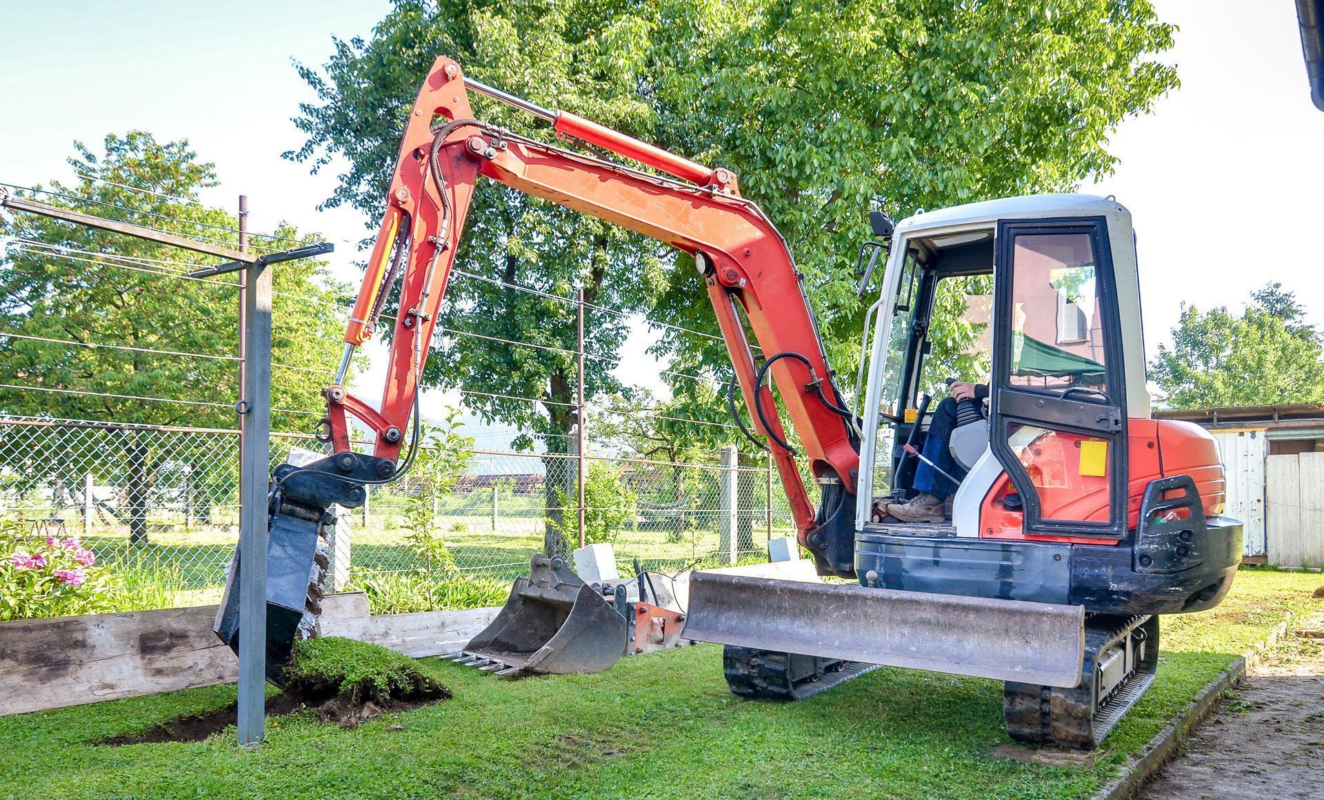 Orange excavator digging in a grassy area next to a clothesline.