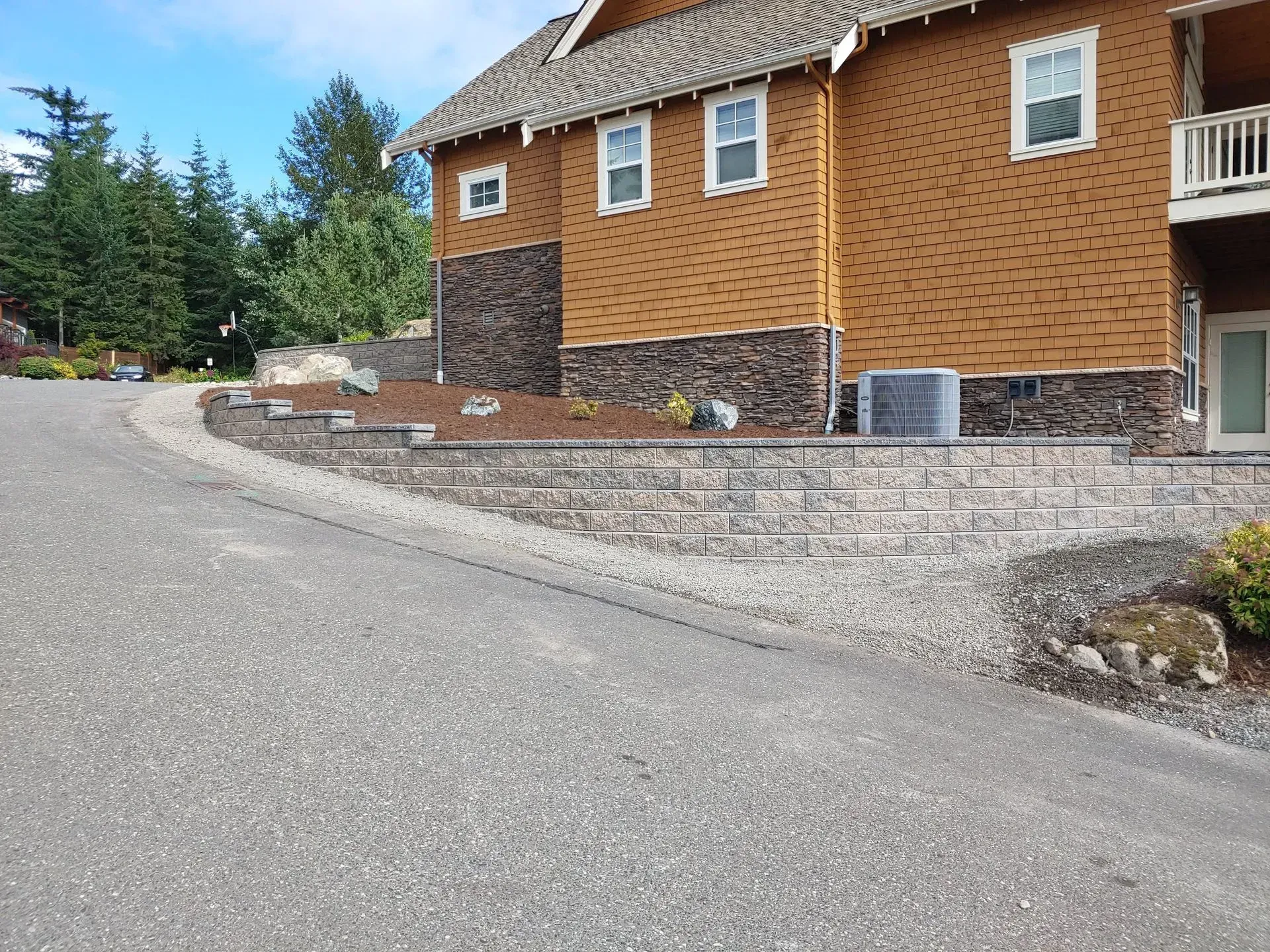 Brown house with stone retaining wall and asphalt driveway.