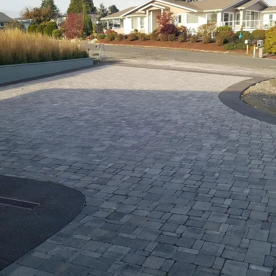 Grey paver driveway curves past a dark asphalt border and into a residential area.