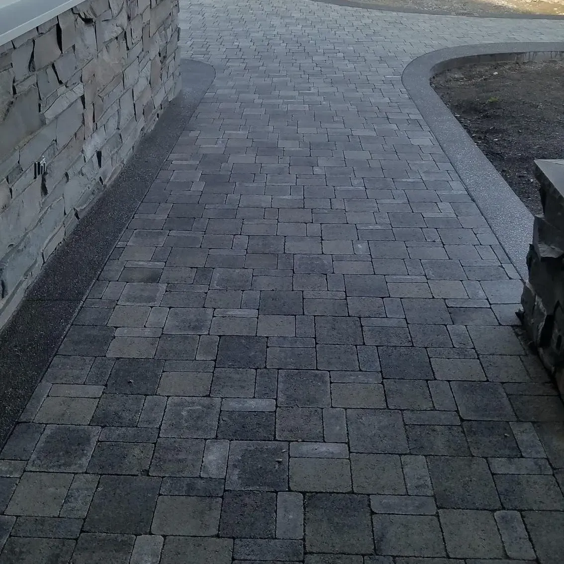 Gray brick pathway next to a stone wall and curved concrete border.