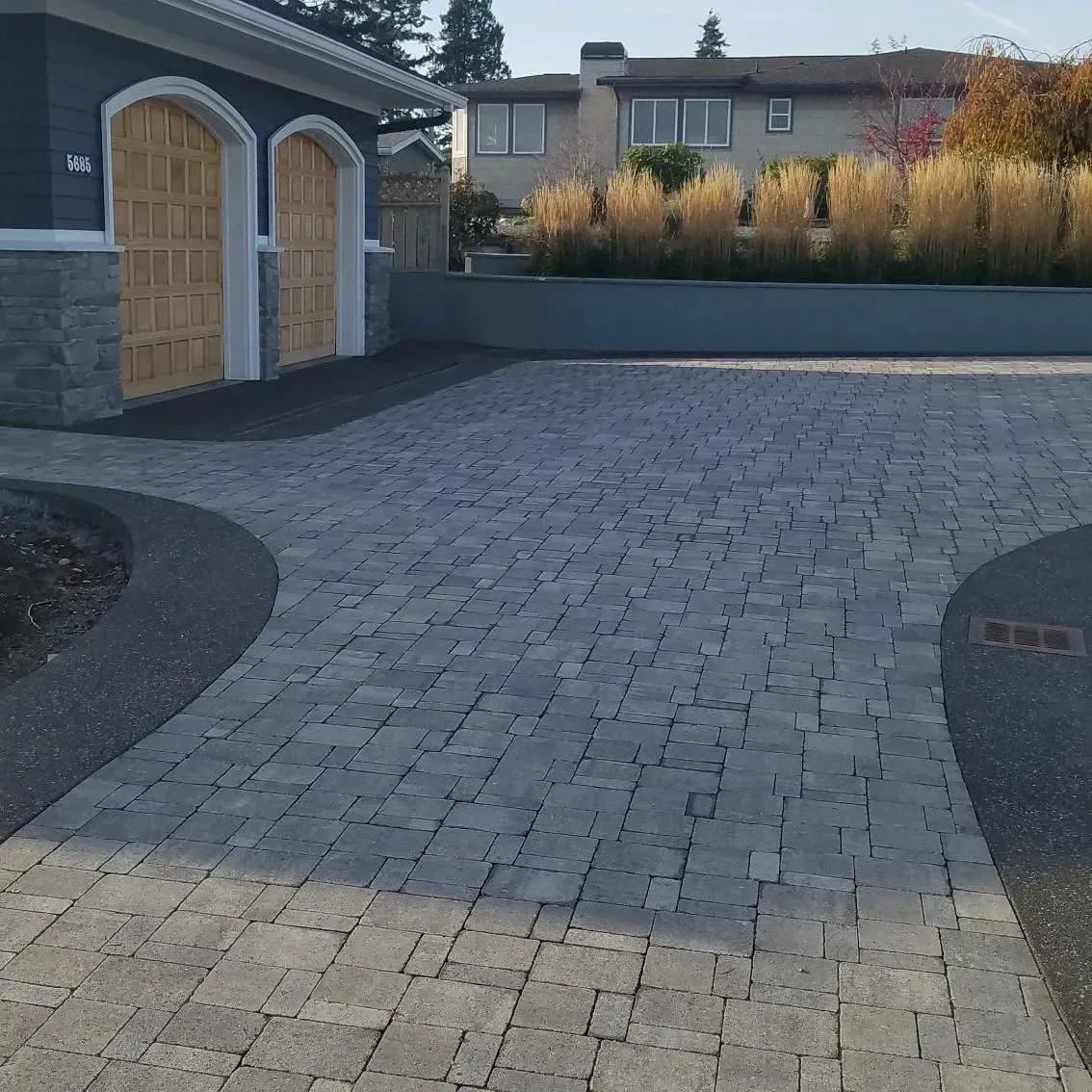 Driveway paved with gray rectangular pavers, leading to a garage with wooden doors.