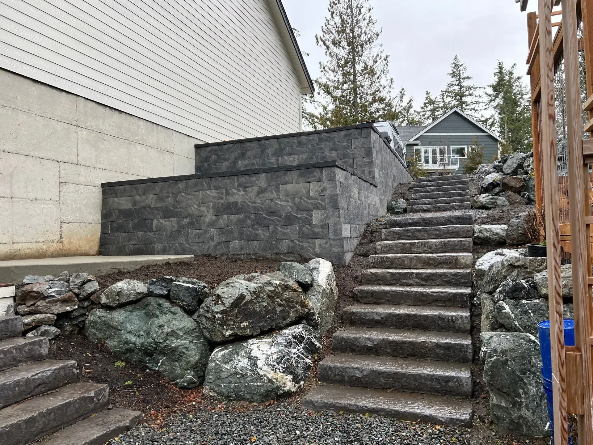 Stone steps lead up a hillside next to a retaining wall and building.