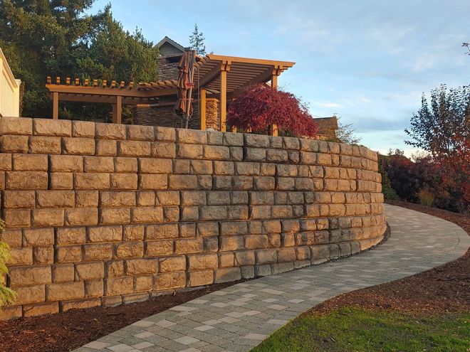 Stone retaining wall with curved path and wood pergola in the background.