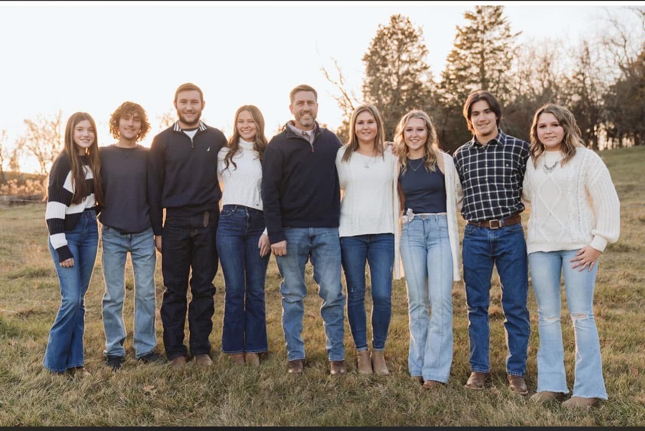 Family of six poses outdoors in autumn; foliage surrounds them.