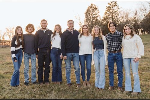 Family of six poses outdoors in autumn; foliage surrounds them.