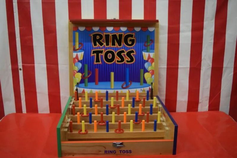 Ring toss carnival game on a red table against striped backdrop.