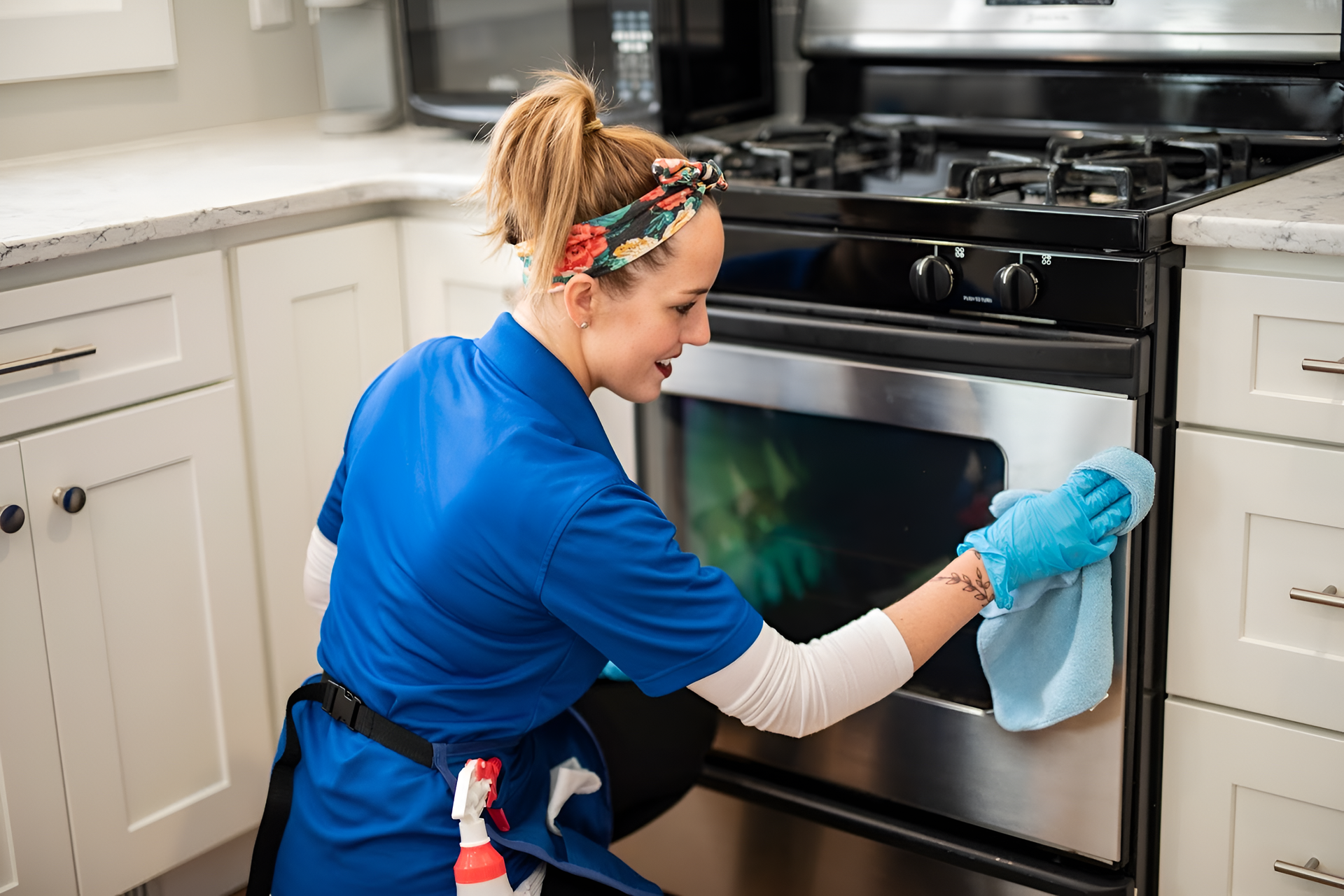 Person in yellow gloves vacuuming a grey sofa in a bright room with a potted plant.