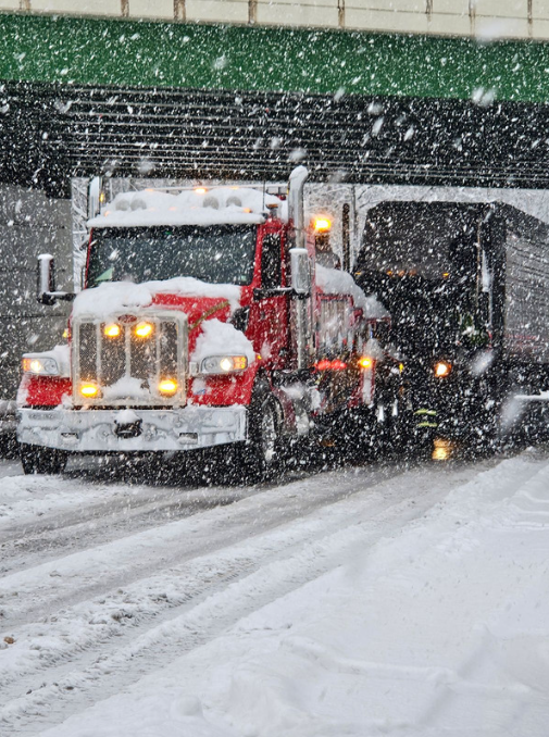 A red and white semi truck is driving down a snowy road