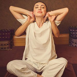 A woman is sitting in a lotus position with her hands behind her head.