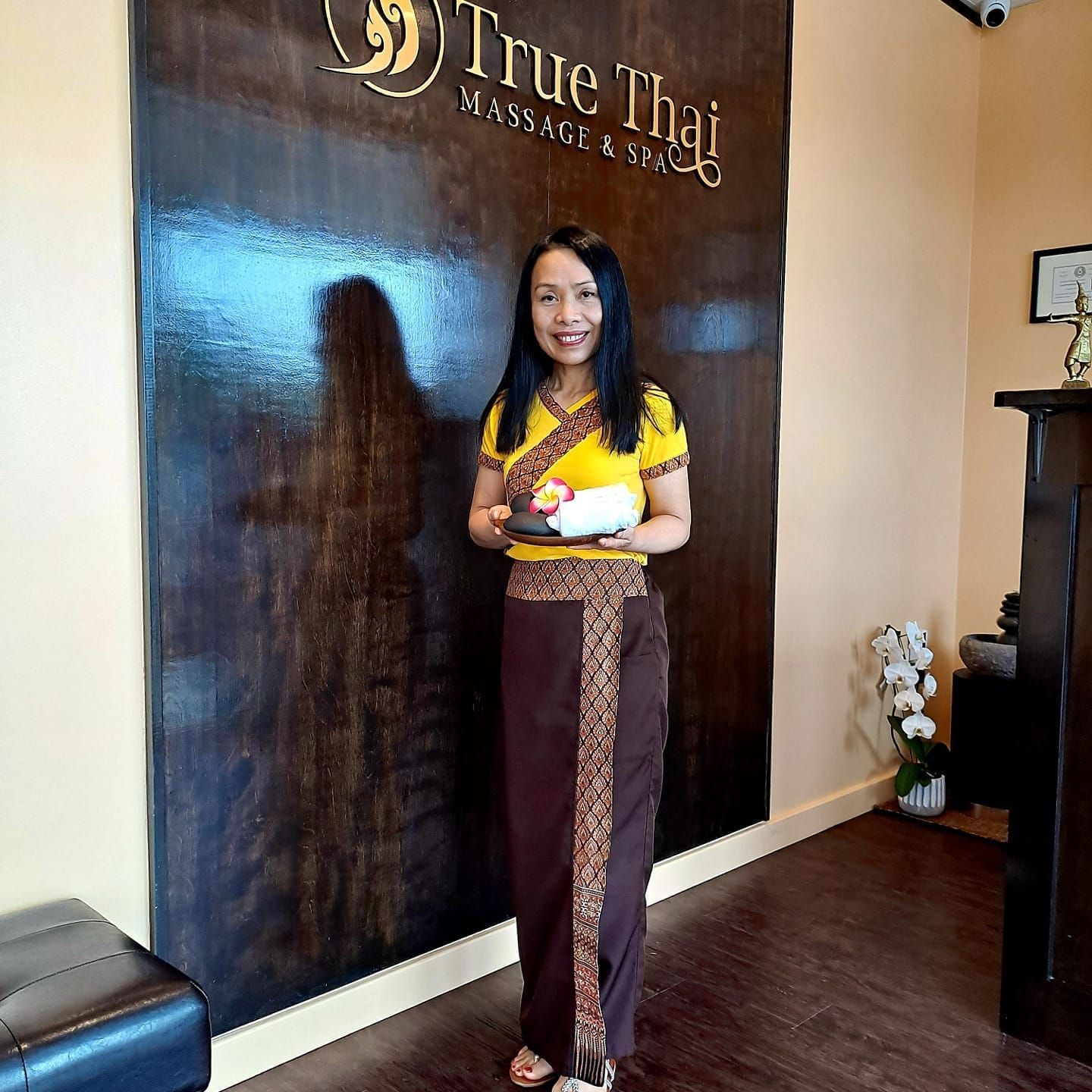 A woman is standing in front of a wall that says true thai