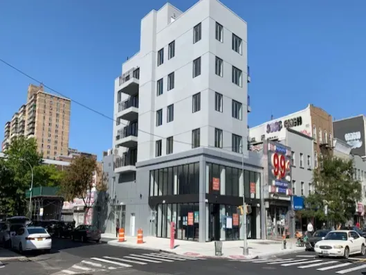 White modern corner building on a city street with parked cars and clear blue sky