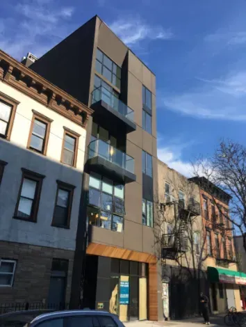 Modern narrow apartment building with glass balconies on a sunny city street.