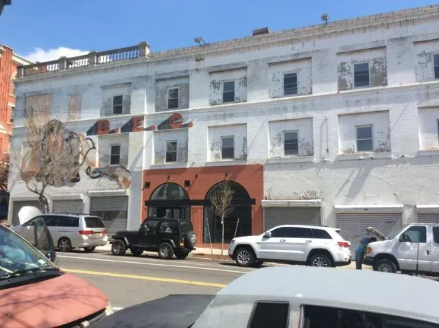 White three-story building with parked cars on a sunny street, featuring a red-orange storefront arch.