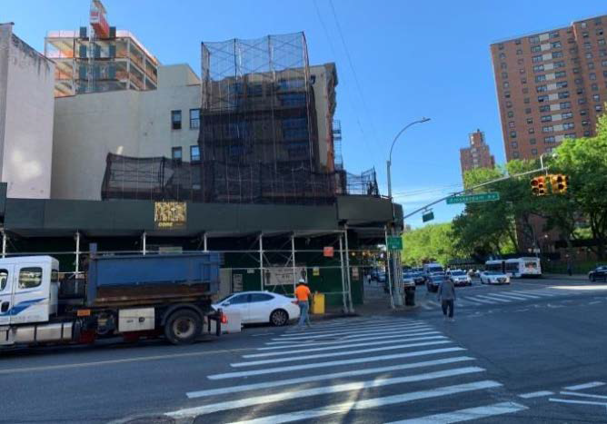 Street intersection with a truck, white car, pedestrians, and a building under construction on a sunny day