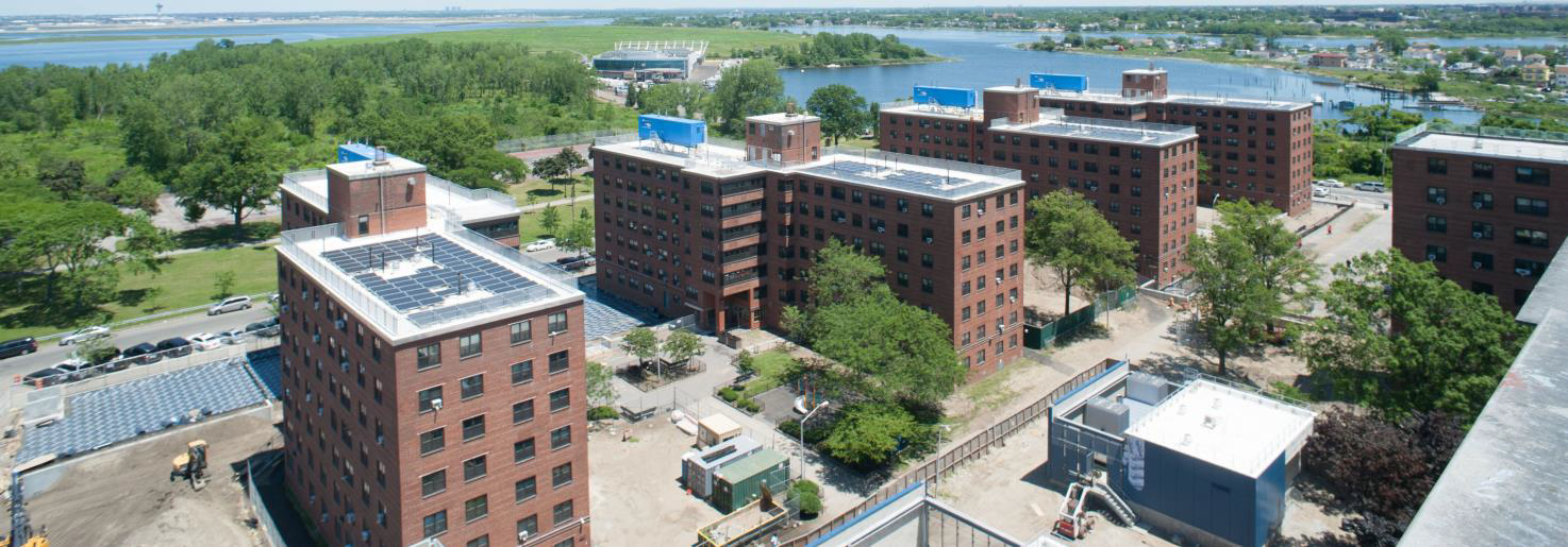 Aerial view of brick apartment buildings near a river, with green trees and streets below