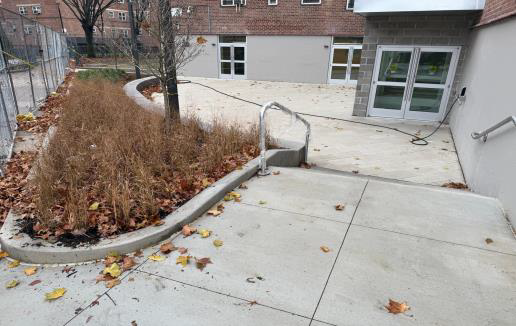 Concrete courtyard with raised planter, fallen leaves, and building entrance with garage doors.