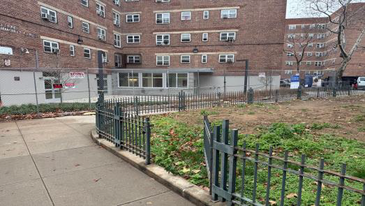 Urban courtyard beside brick apartment buildings, with a fenced garden and sidewalk path.