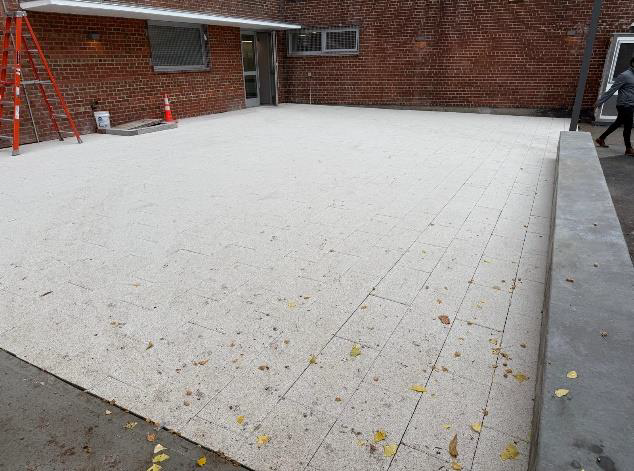Snow-covered brick courtyard with a ladder and cones beside a building