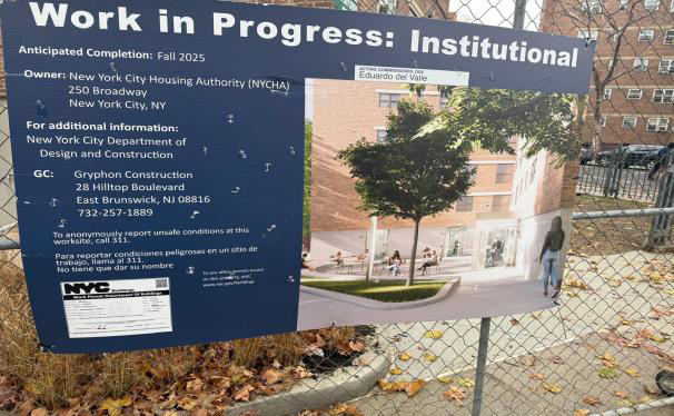Work in Progress sign for institutional building, blue board beside chain-link fence and construction site.