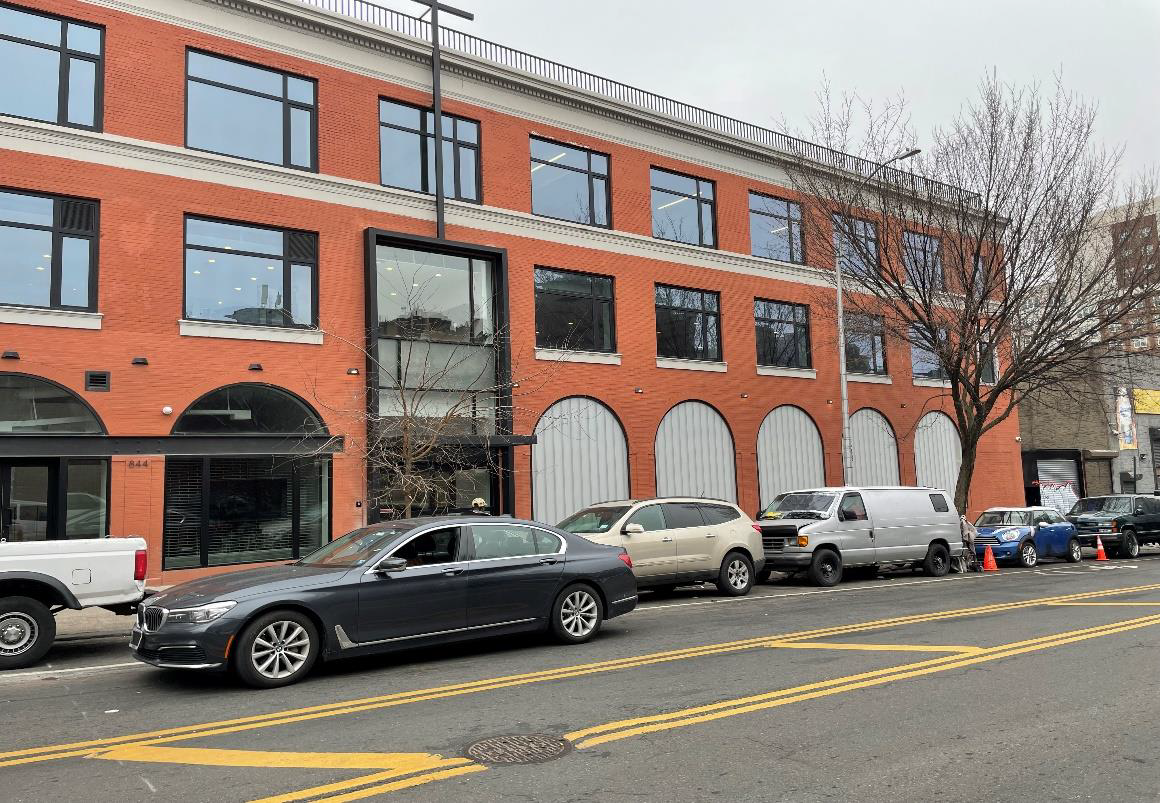 Brick office building with parked cars along a city street under overcast skies