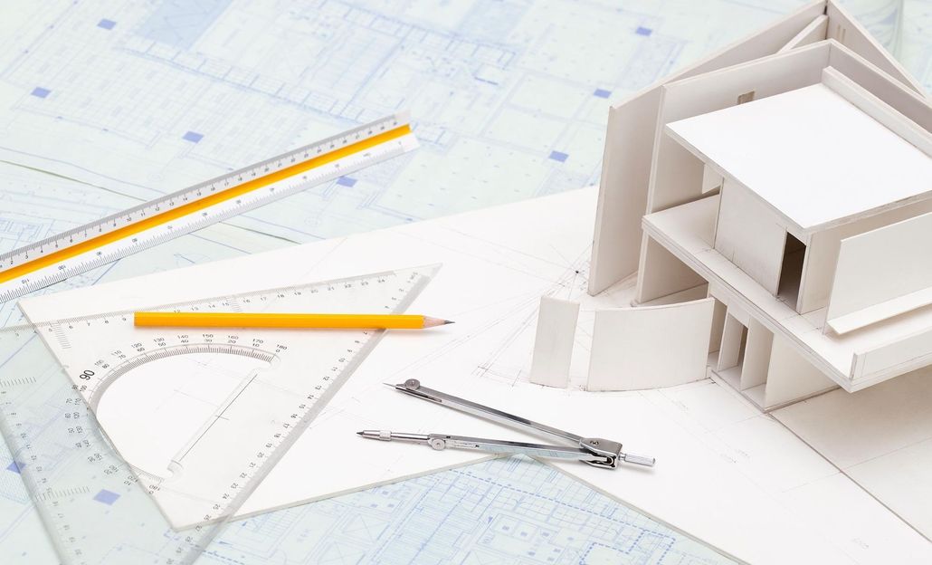 Architectural model with pencils, ruler, protractor, and blueprint plans on a drafting table