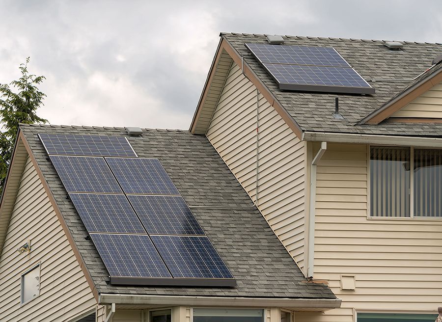 A one-story tan house with a white roof and solar panels, featuring a two-car garage and landscaped green bushes in front.