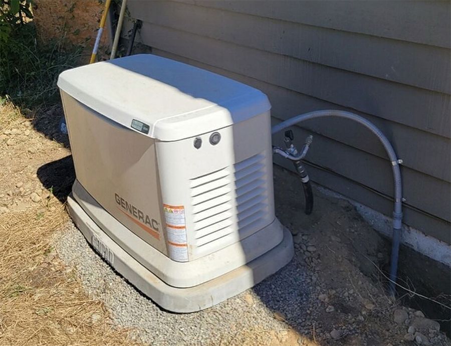 A light gray outdoor home standby generator sits on a concrete pad surrounded by several residential HVAC units.