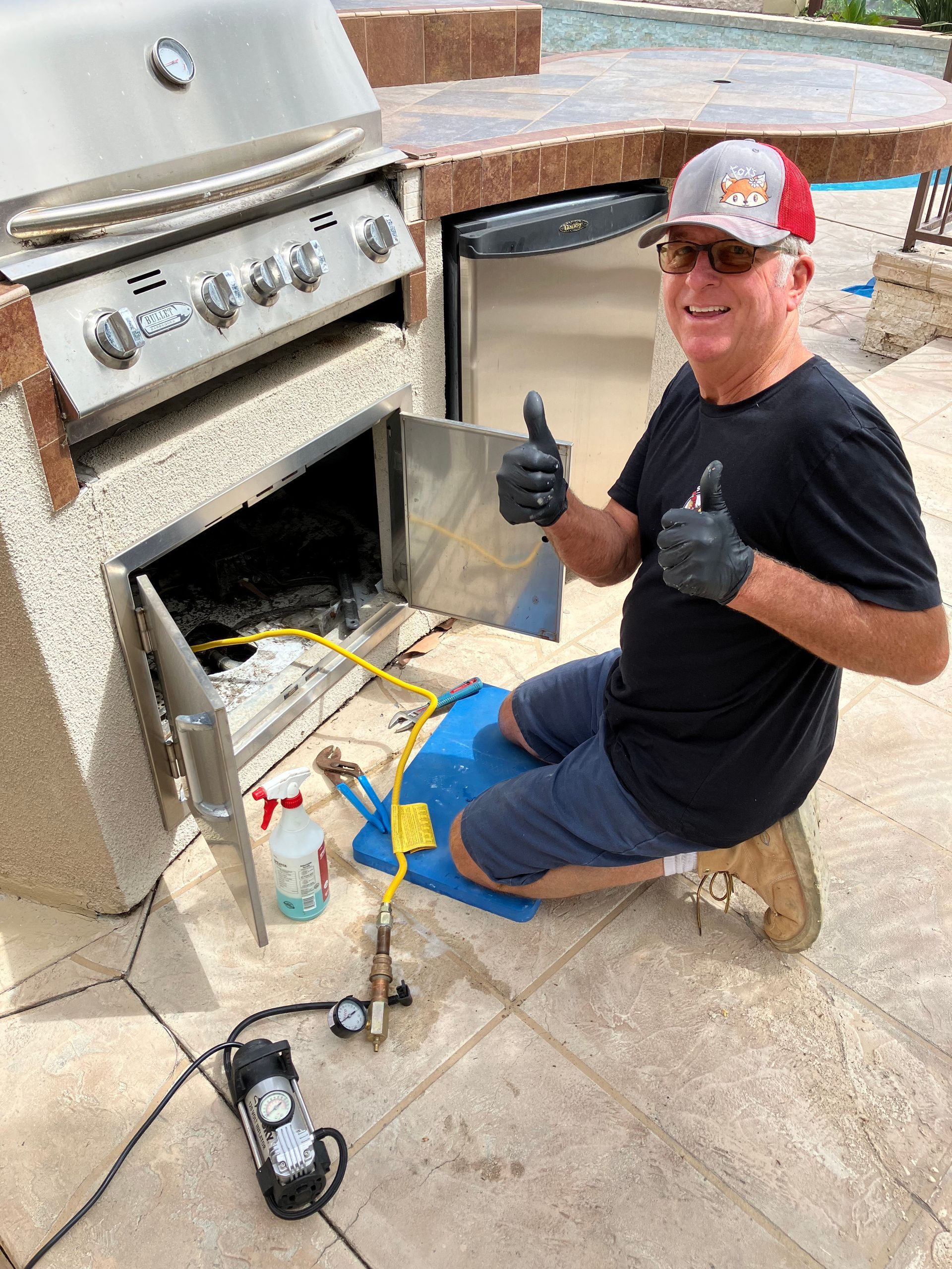 A man is kneeling down in front of a grill and giving a thumbs up.