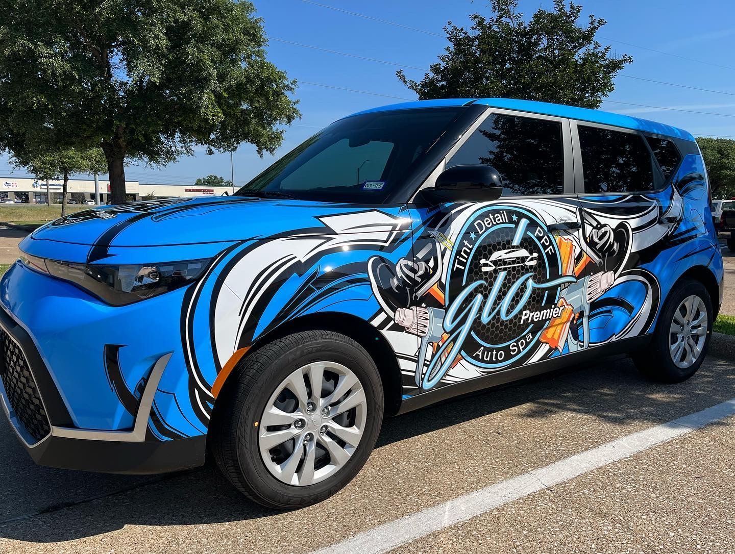 a blue car with a wrap on it is parked in a parking lot .