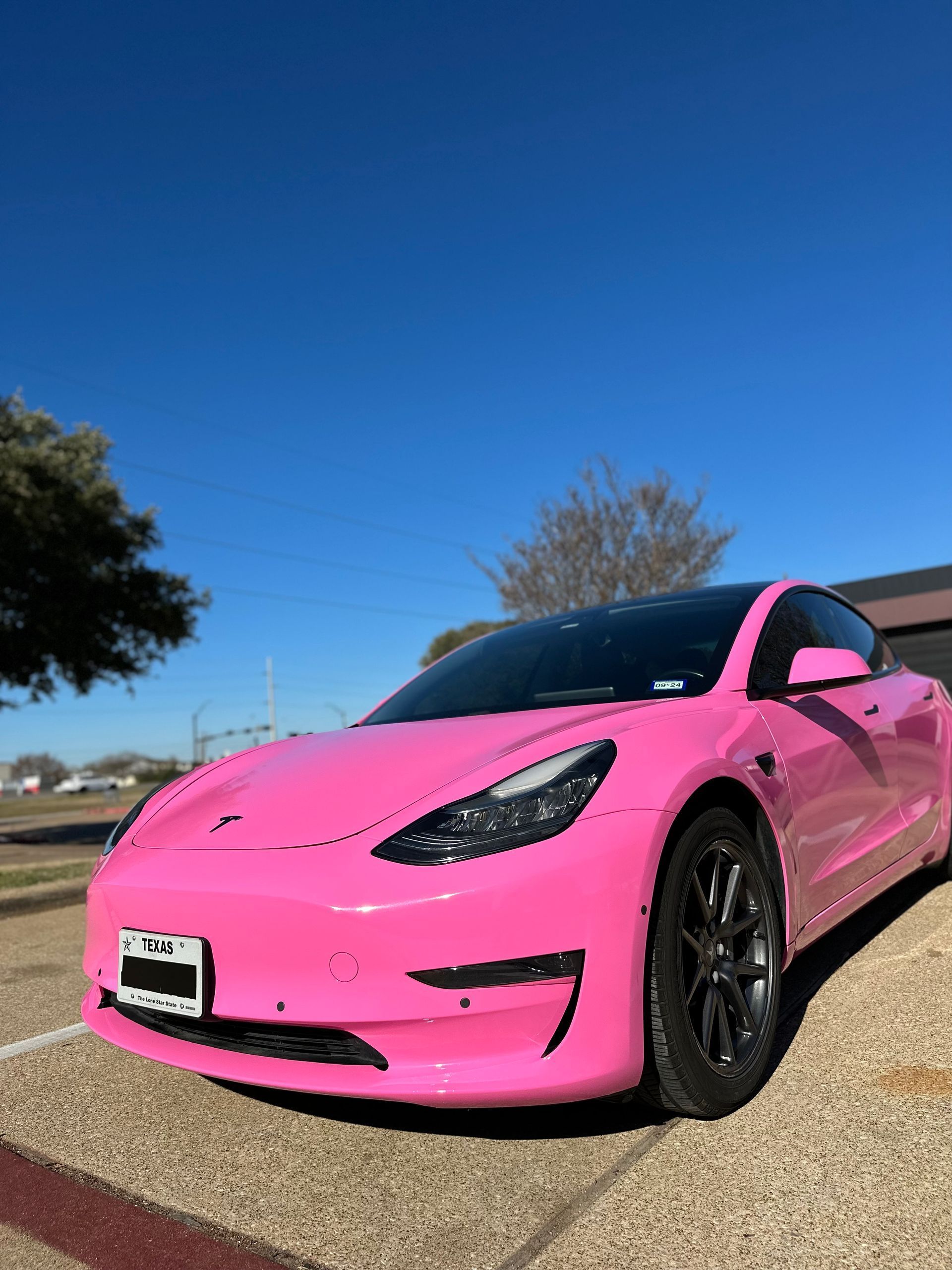 a pink tesla model 3 is parked in a parking lot.