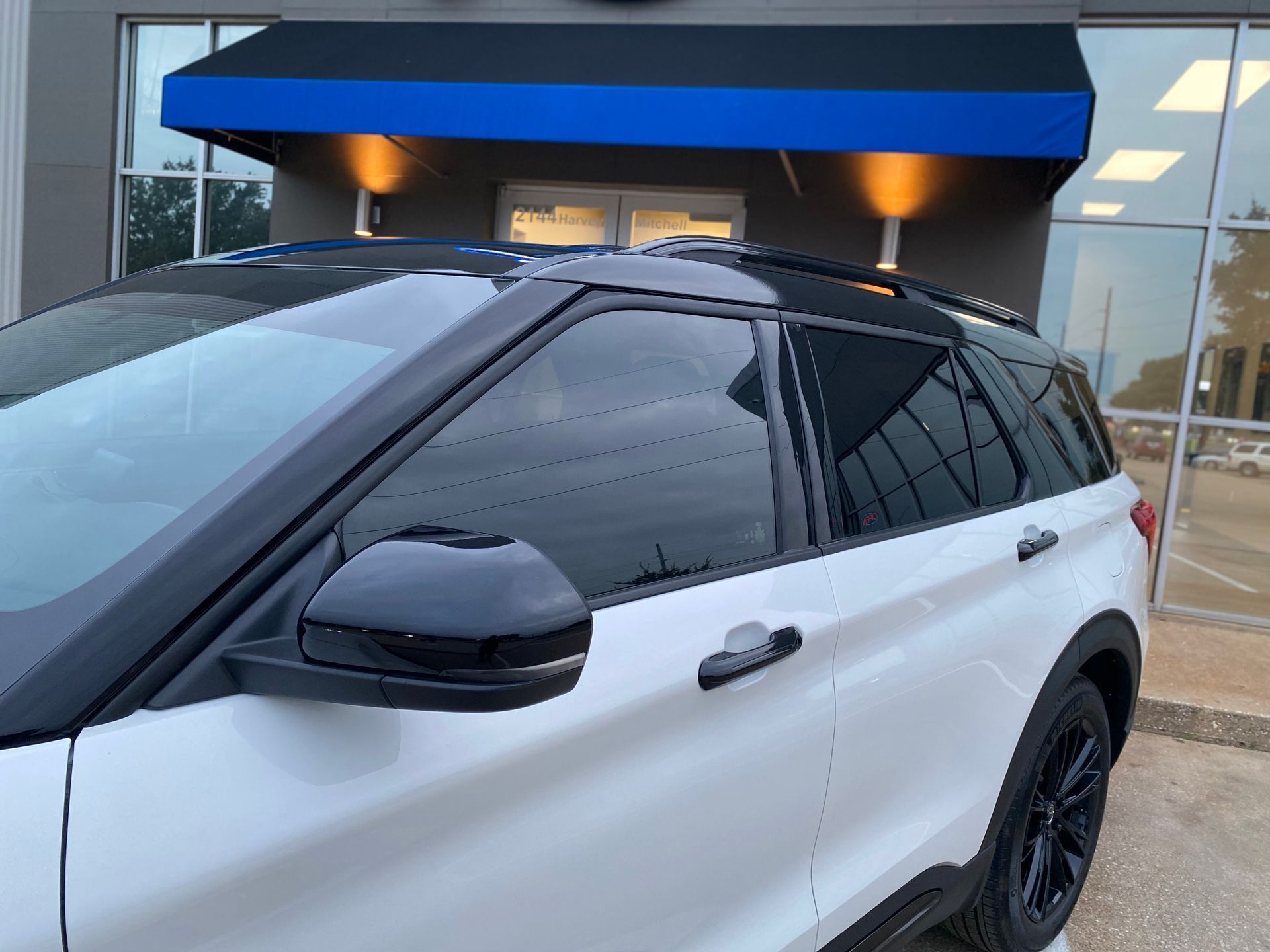 a white SUV is parked in front of a building with a blue awning.