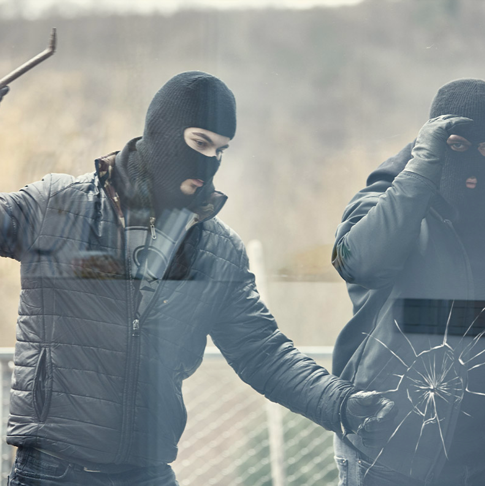 A man in a mask is breaking a window with a crowbar