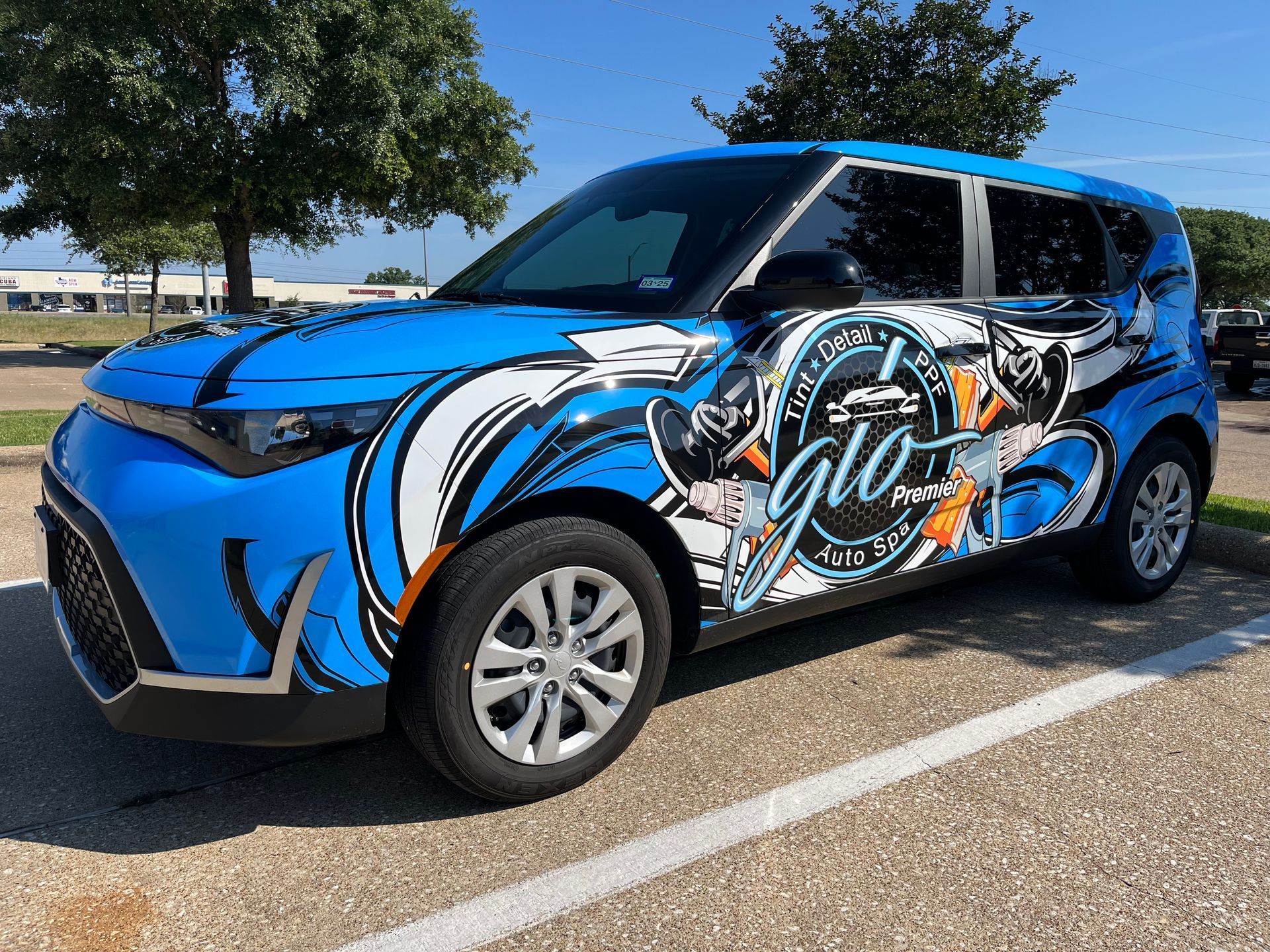 a blue car with a wrap on it is parked in a parking lot .