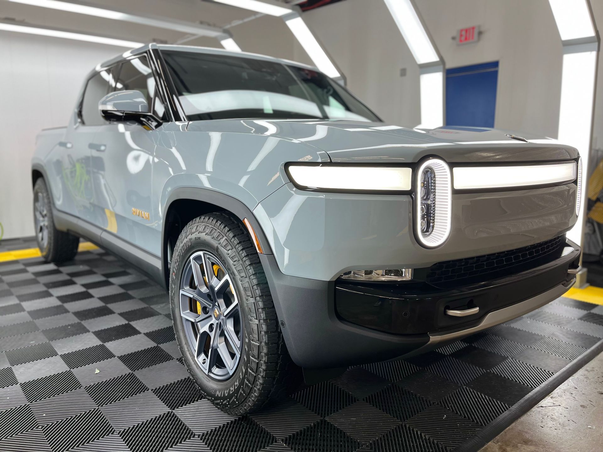 a gray rivian pickup truck is parked on a checkered floor in a garage .
