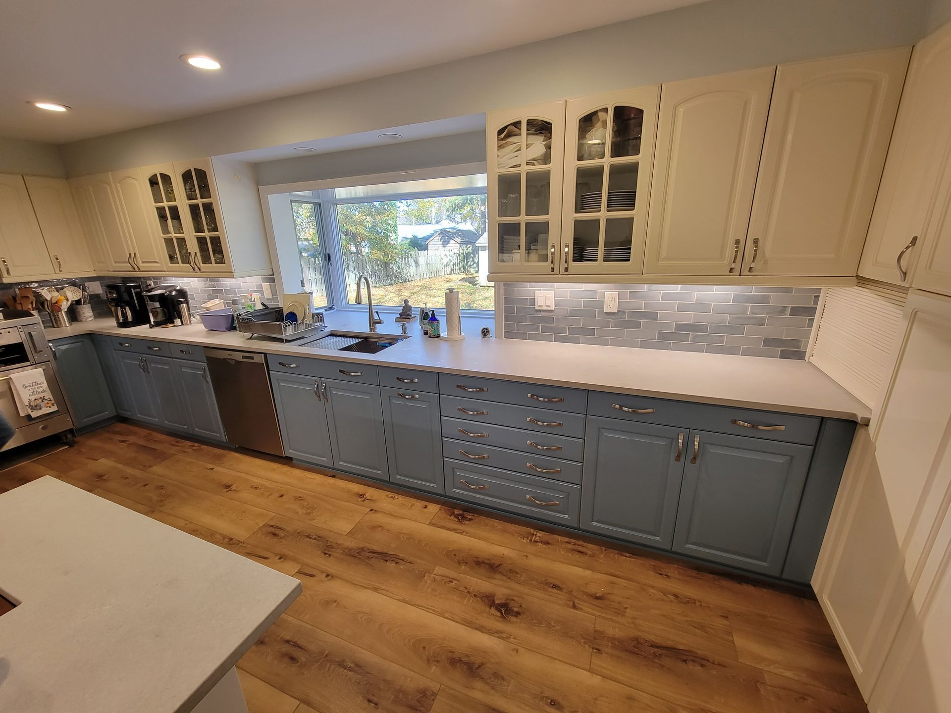 A kitchen with blue cabinets, white counter tops, a sink, and a window.