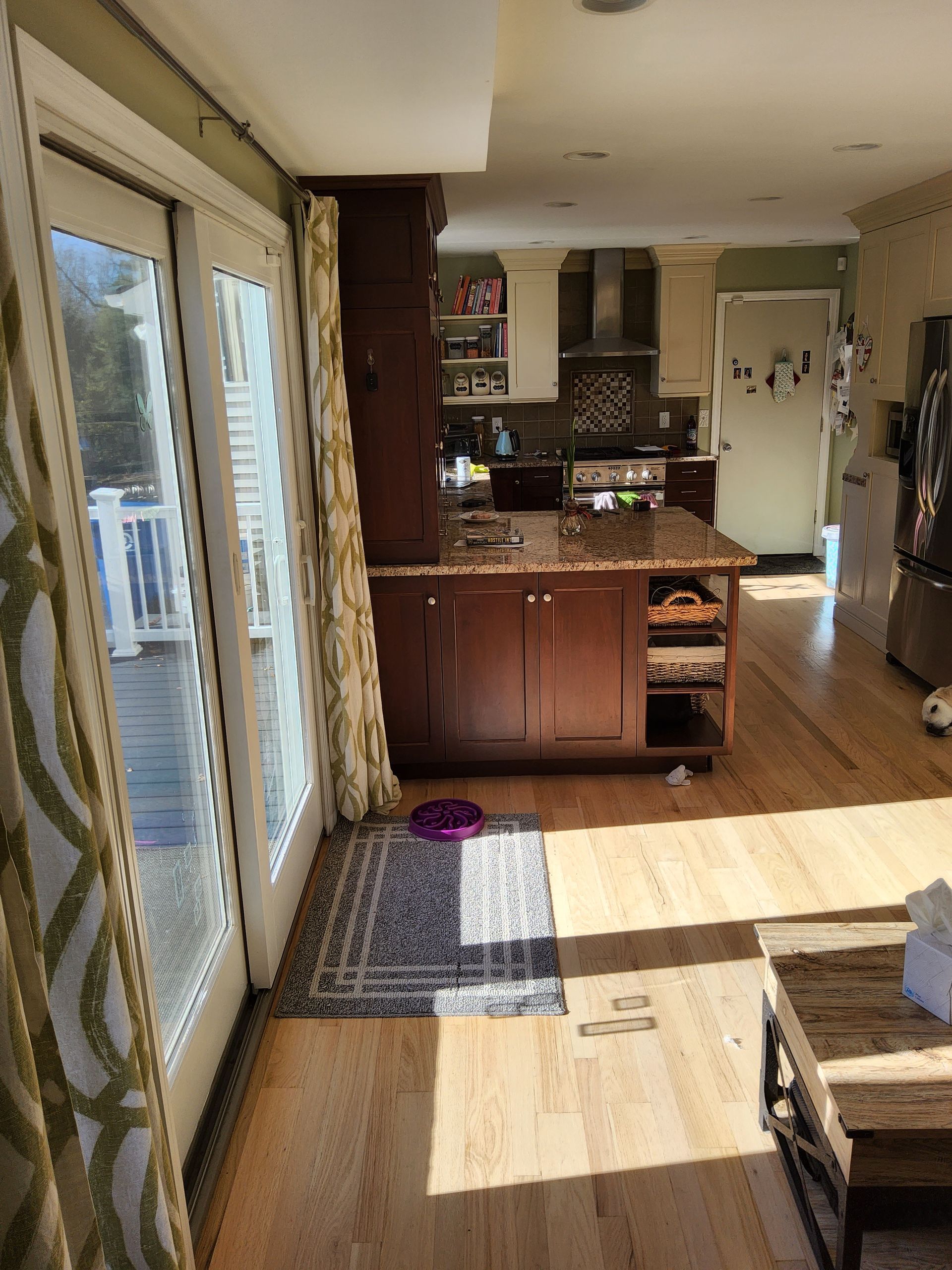 A living room with hardwood floors and sliding glass doors leading to a kitchen.