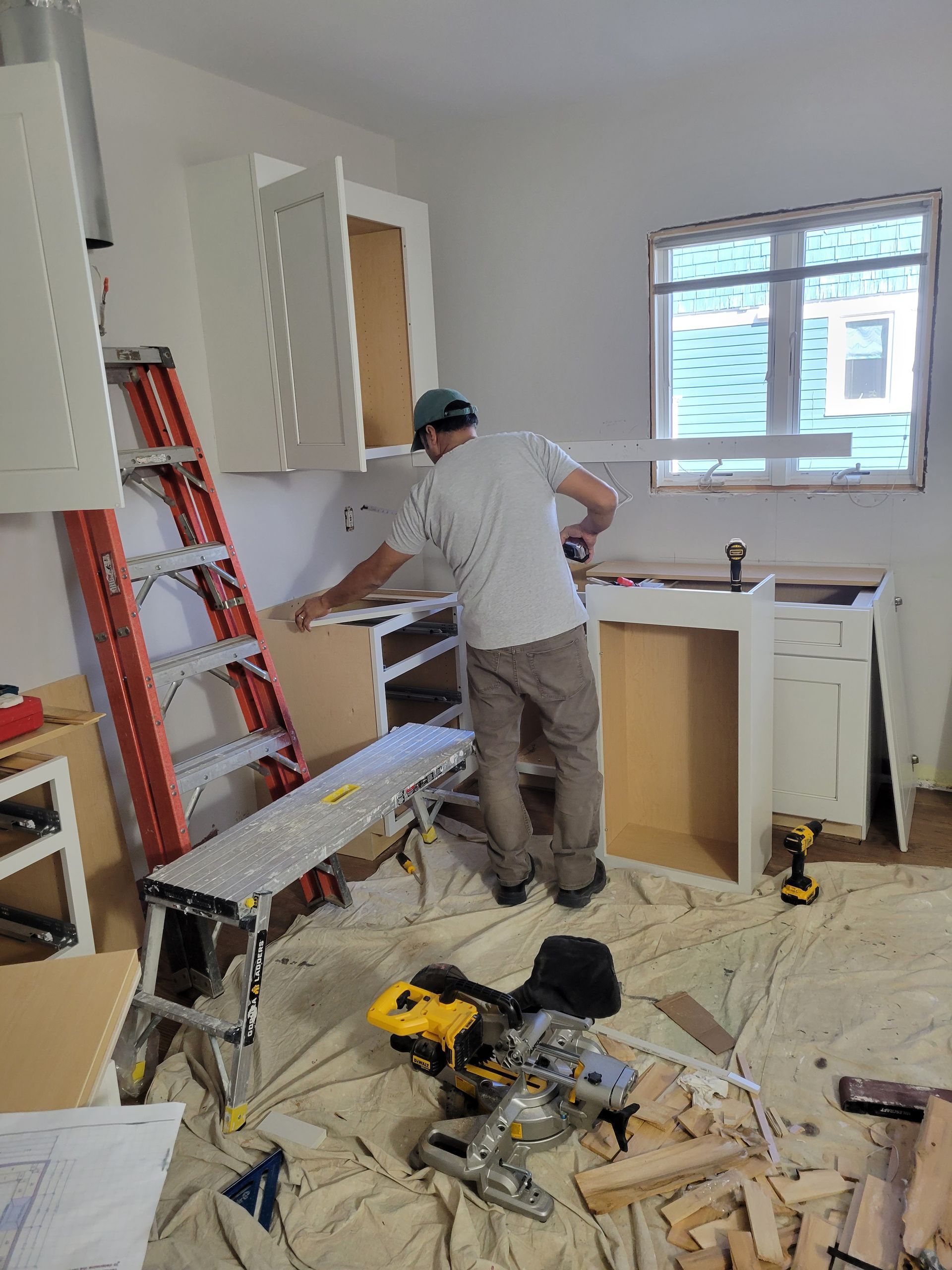 A man is working on a kitchen with a ladder in the background.