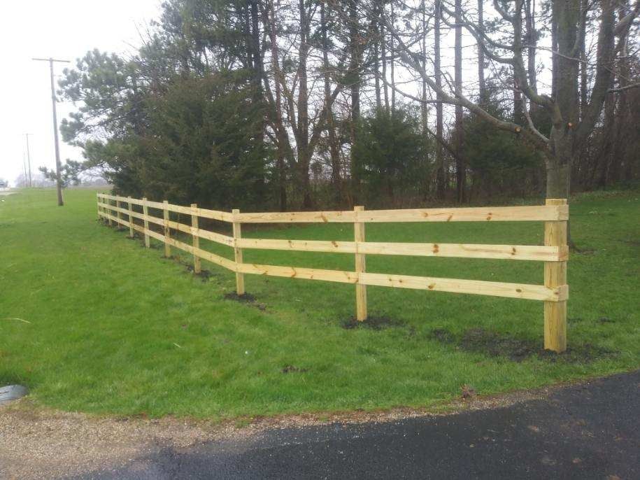 Wooden fence on a green lawn, near trees.