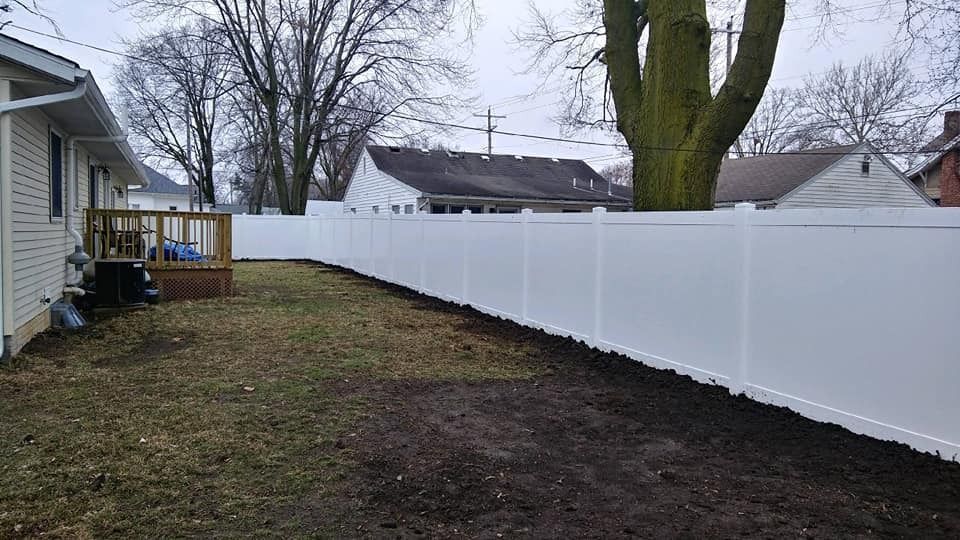 Backyard with white fence, brown grass, and bare trees.
