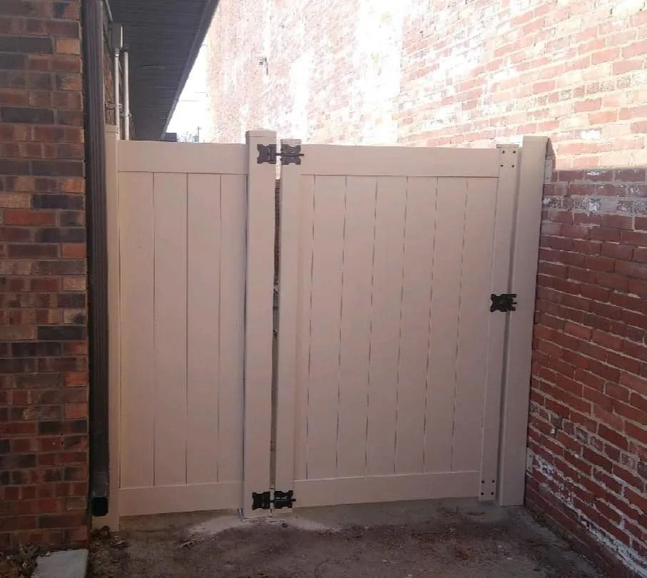 Beige wooden gate between brick walls, with black hinges and latch.