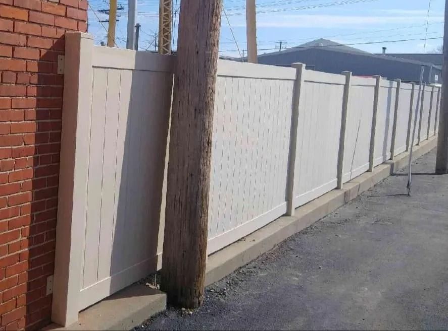 Beige vinyl fence next to a brick wall and a wooden utility pole.