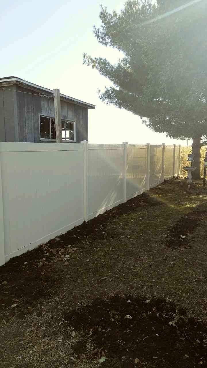 White fence next to a weathered building and tree under a bright sky.